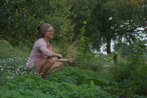Laure, productrice de plantes médicinales, accroupie dans son jardin en été, souriante.